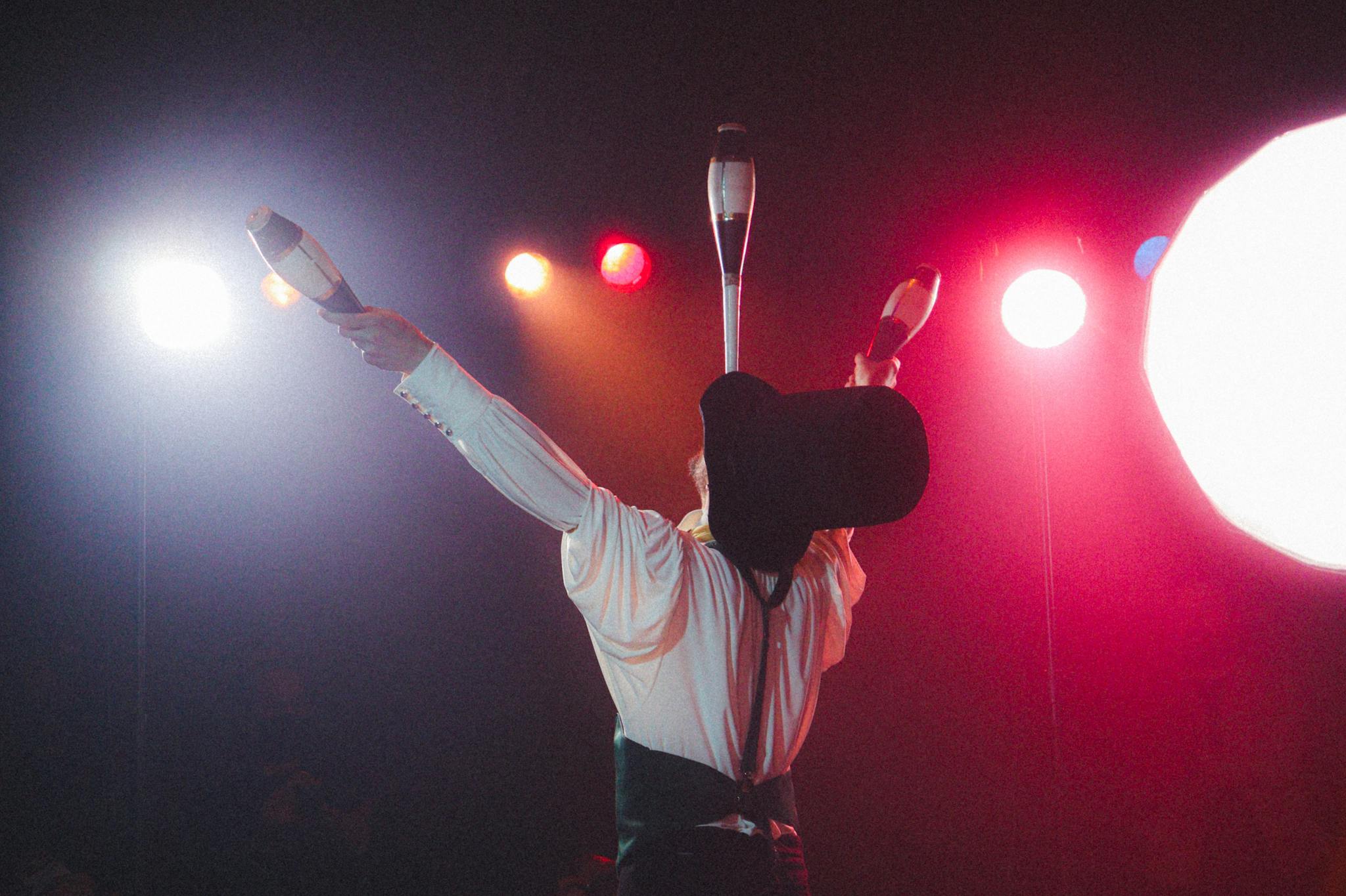 Dramatic shot of a circus performer skillfully juggling clubs under vibrant stage lights.