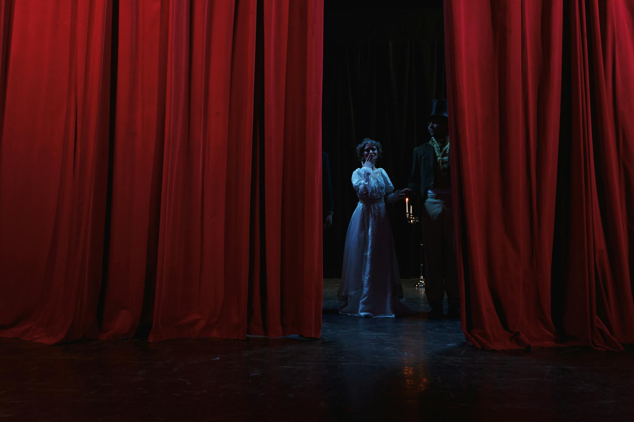Dramatic stage scene with actors behind red curtains, creating a theatrical ambiance.