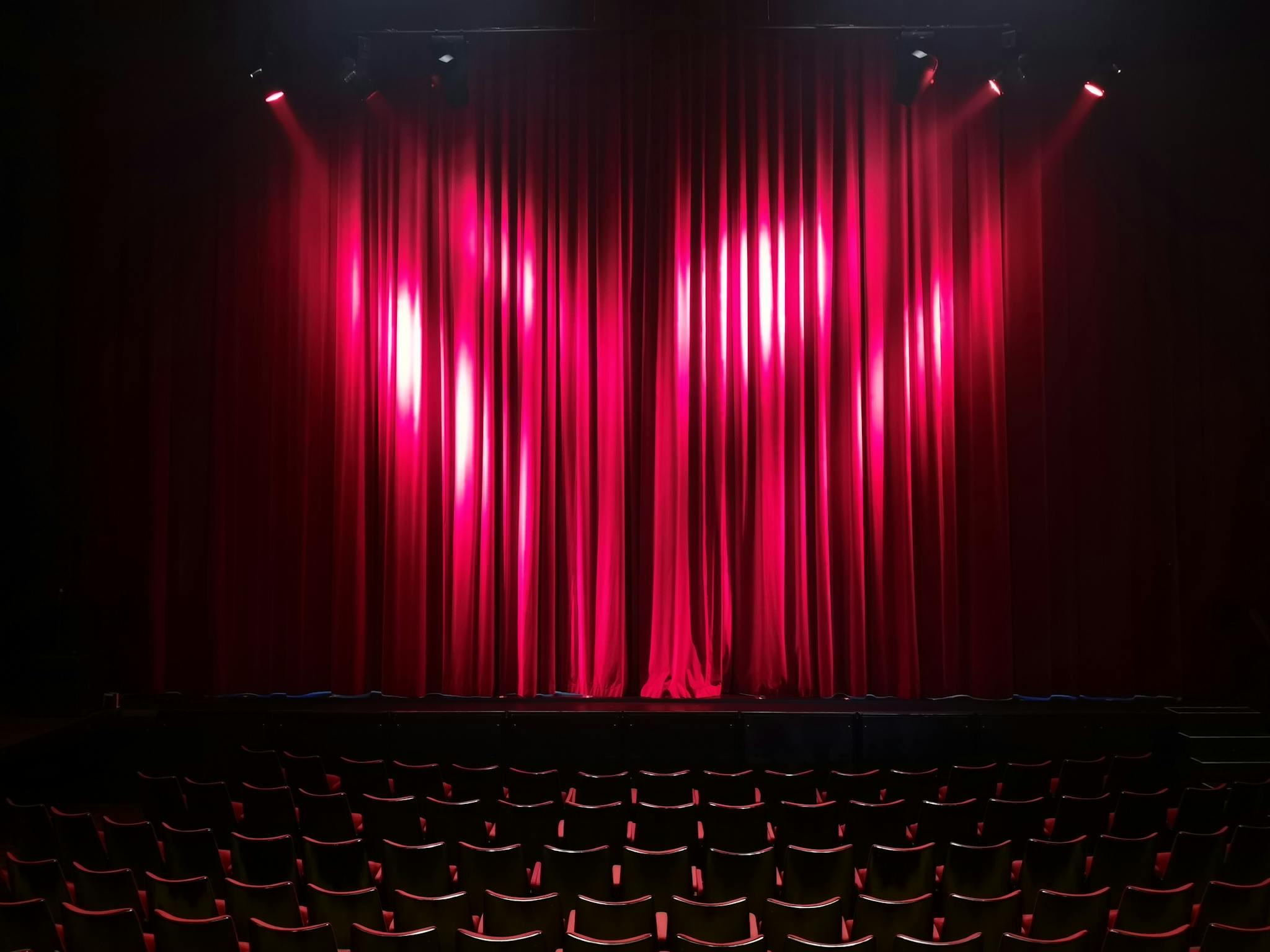 Empty theater stage with red curtains and seating, ready for a performance.