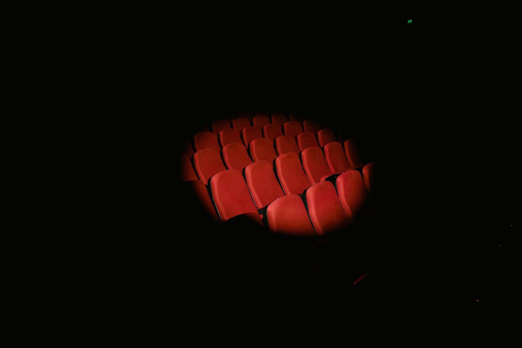Rows of red theater seats spotlighted in a dark auditorium, evoking a cinematic atmosphere.