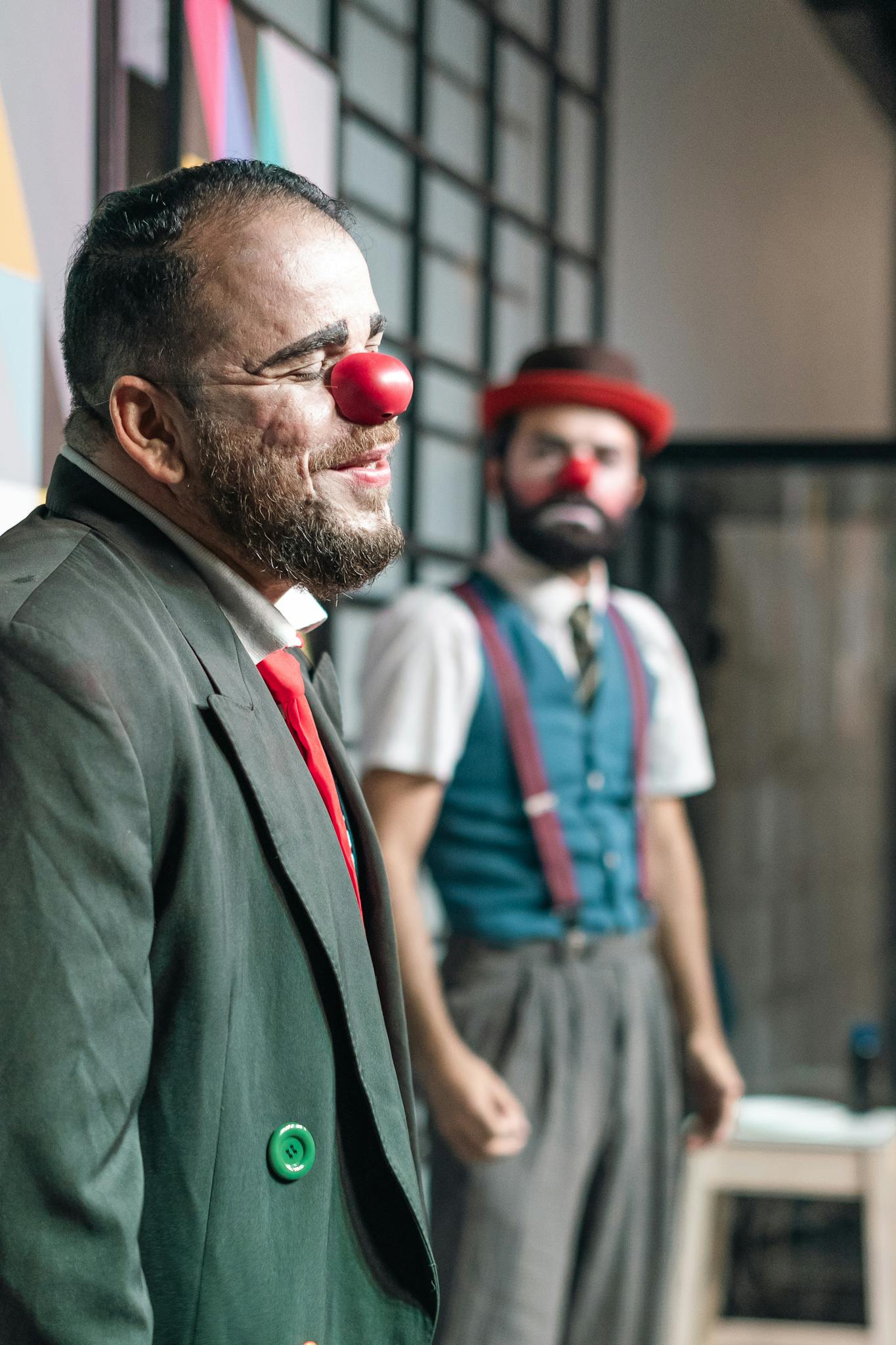 Two clowns with red noses performing in a theatrical setting, smiling and engaging with the audience.
